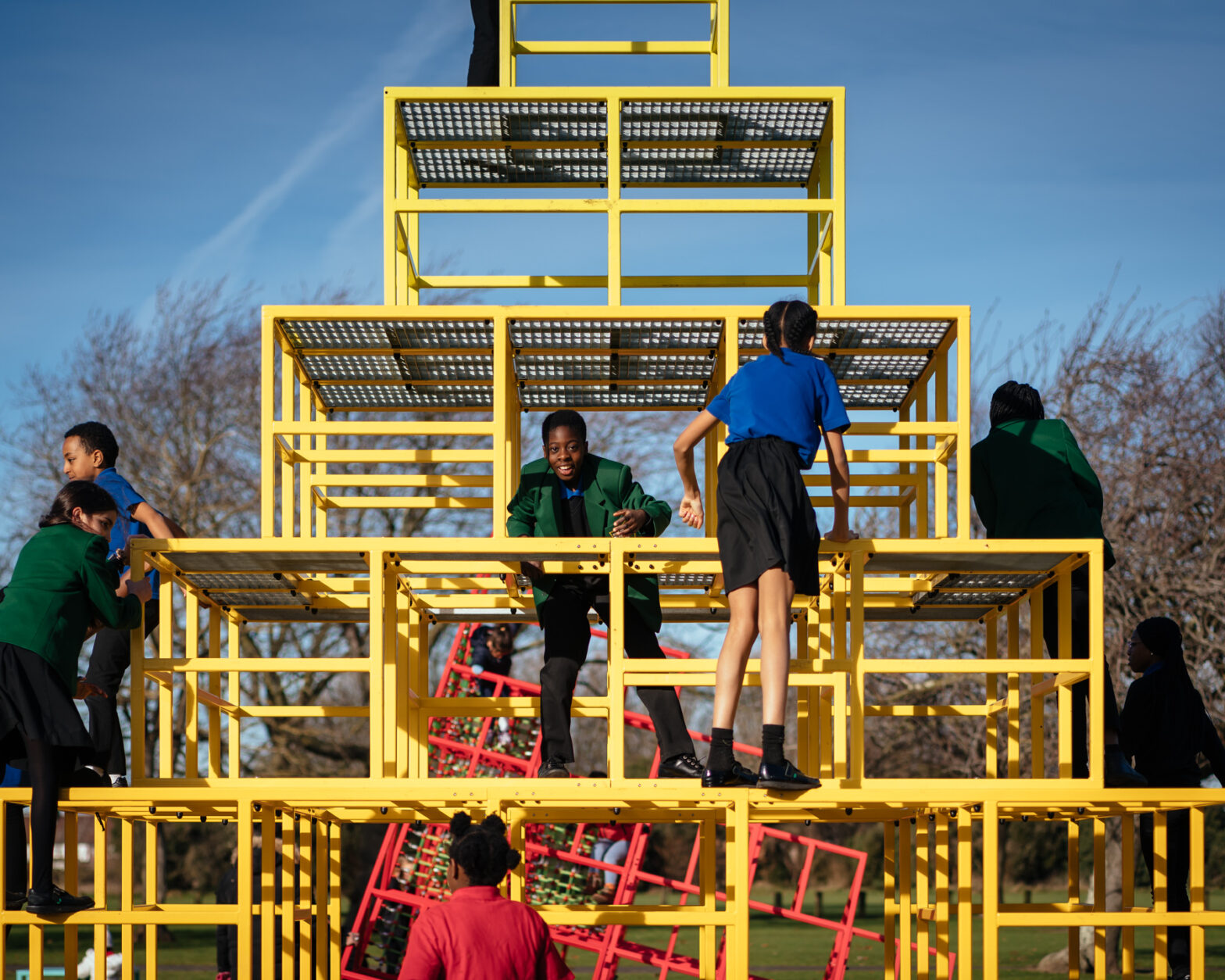 Photograph of the artwork: Eva Rothschild, 'Parsloes Memphis' playground. - Some children on a climbing frame which is the form of pyramid constructed from yellow tubular metal.